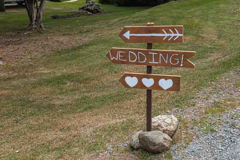 A wooden wedding sign pointing the guests to the wedding ceremony location.
